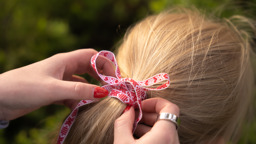 Händer knyter ett rött och vitt band i en fläta på ett barns hår.